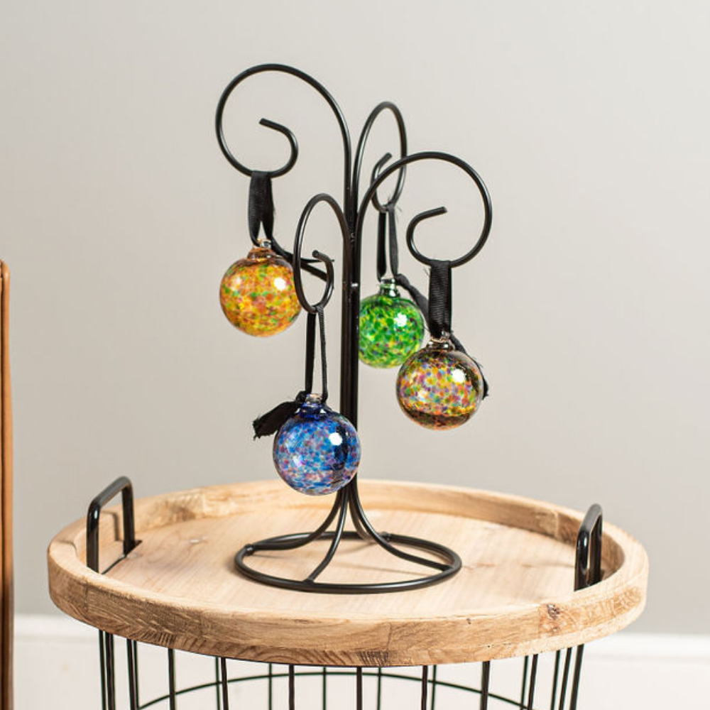 Four balls in oranges, greens, blues and multicolours on a black four ornament stand. Displayed on a side table. 