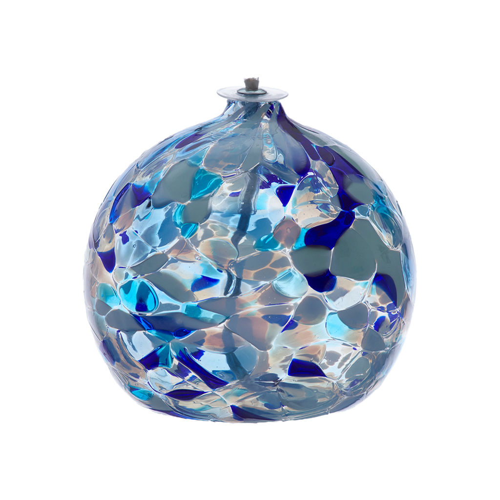 Round glass ball with flat base and wick with opaque blue, light blue and opaque white glass mosaiced around the entire surface on a transparent background.