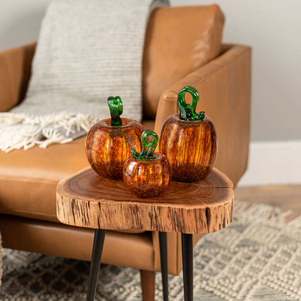 3" and 6" Round and Oval Rust Pumpkins on an end table in front of a brown leather chair with a grey blanket. 