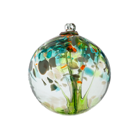 Clear glass orb with lime glass pulled through the middle and yellow, green, gold glitter and blue glass bits on top on a transparent background